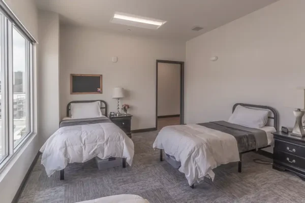 Men’s bedroom with four beds per room, plus a side table and under-bed storage bin for each male patient.